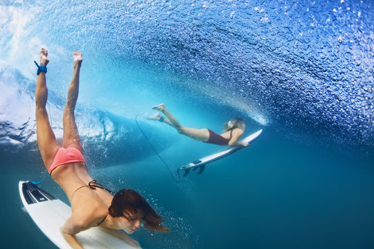 Active girls in bikini in action - surfers with surf board dive underwater under breaking big ocean wave. Family lifestyle, people water sport adventure camp, beach extreme swim on summer vacation