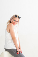 Cheerful blonde model smiling at camera while sitting, white background. Beauty portrait, perfect makeup. Sexy fashion woman
