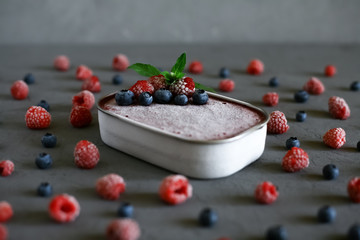Raspberry and blueberry homemade ice cream in a metal bowl, decorated with raspberries, blueberries and mint on a gray background