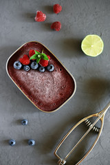Raspberry and blueberry homemade ice cream in a metal bowl, decorated with raspberries, blueberries, mint and Ice-cream scoop, raspberries, blueberries and lime on a gray background, flat lay