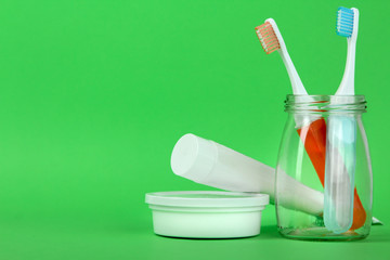 Toothbrushes in a glass jar near the toothpaste on a green background
