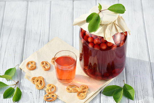 Homemade cherry preserved canned compote in glass with cookies on white wooden table in garden