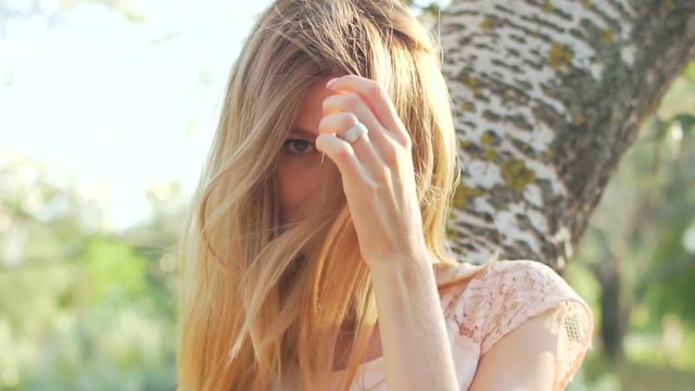 Portrait of beauty young blonde while she sitting on the tree branch, smiling and posing to camera