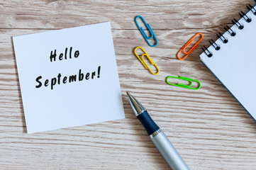Hello September wrote at paper sticker on wooden workplace background