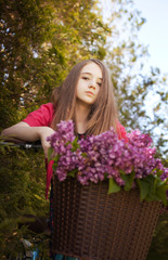 Beautiful teenage girl sitting on a bicycle with a basket of flowers
