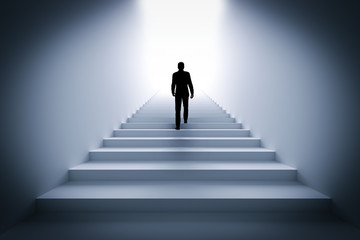 Businessman climbing the stairs towards light.