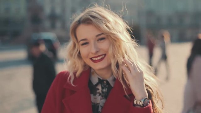 Attractive young woman with red lips in the city turning to camera and smiles. Steady cam shot, slow motion.