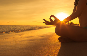 Yoga concept. hand woman practicing lotus pose on the beach at sunset.

