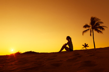 Fototapeta na wymiar Young woman relaxing on a tropical beach watching the sunset. 