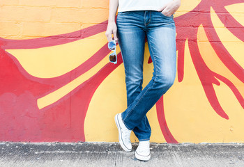 Girl posing in jeans and sneakers against a colorful background. 