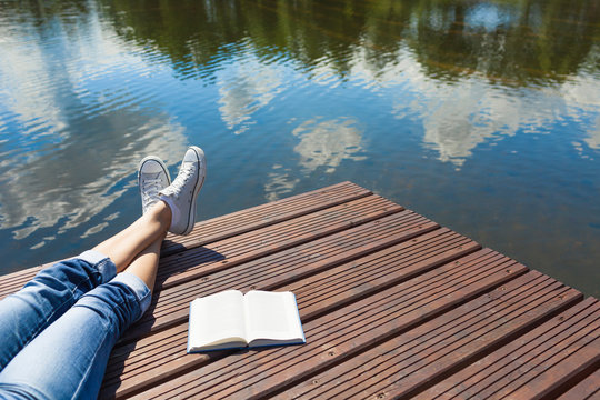 Relaxing and vacation and reading concept. Woman relaxing by the waters edge with a book by her side. 