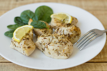 Baked chicken fillet with lemon slices and spinach leaves on a white simple plate