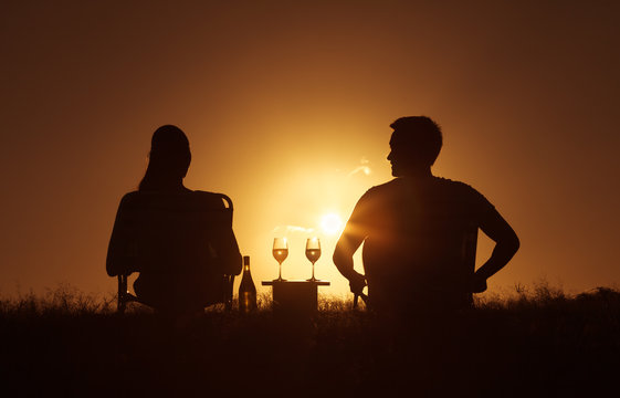 Young couple sitting in the park enjoying a glass of wine and a beautiful sunset. 