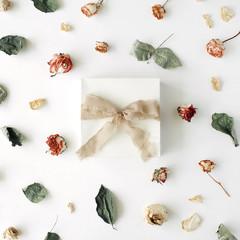white gift box with brown ribbon and bow on white decorated with roses and dry leaves background. flat lat, top view