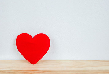 Red heart on wooden table and white wall with vintage tone