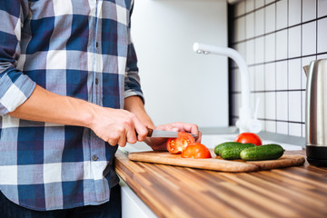 Closeup of man standing and cutting vegetables on the kitchen
