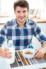 Fototapeta na wymiar Man eating cereals with milk at the table on kitchen