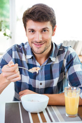 Cheerful man eating cereals with milk for breakfast on kitchen