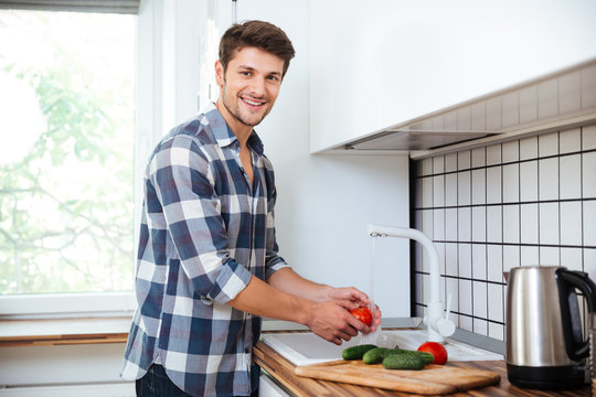 Cheerful young man washing vegetables on the kitchen