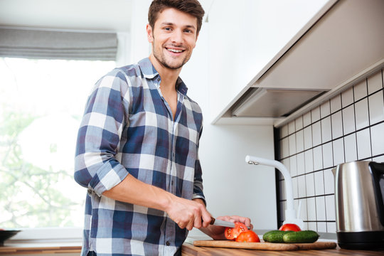 Cheerful young man cutting vegetables for salad on the kitchen