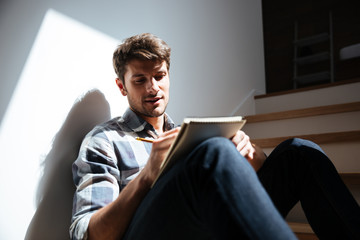 Man sitting on stairs at home and writing in notepad