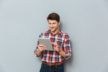 Happy young man in plaid shirt standing and using tablet