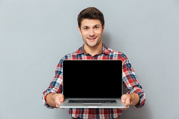 Smiling young man in checkered shirt holding blank screen laptop