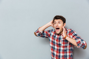 Stunned afraid young man in checkered shirt standing and shouting