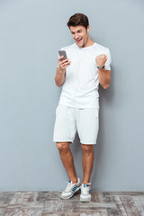 Happy attractive young man with earphones and smartphone celebrating success