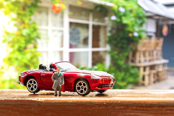 Business figure and toy car with blurred background of clothes shop window