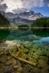 Beautiful reflection of highest mountain peak Zugspitze with old tree under water at Eibsee lake and amazing stormy clouds, Bavaria, Germany.