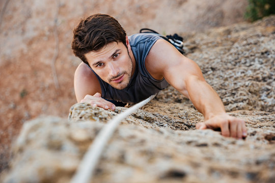 Muscular strong male athlete climbs a steep cliff, rock climbing sport.  Stern look to achieve the goal to climb to the top, a difficult site.  Generative AI Stock Illustration