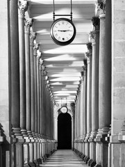 Long colonnafe corridor with columns and clock hanging from ceiling. Cloister perspective. . Black...