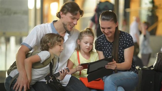 Young mother showing to her family something interesting in tablet PC while they are sitting in airport departure lounge or railway station.
