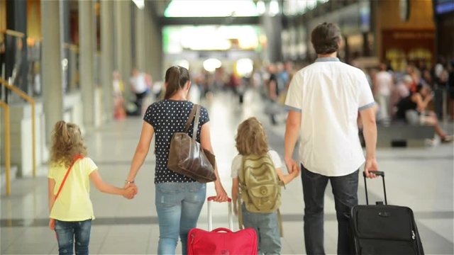 Happy family with little girl and boy going on railway station, mother father and the kids walk through the airport with suitcases
