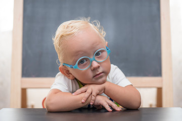 Baby sitting at a table against the background of the easel glasses for vision for chalk drawing