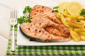 Grilled salmon with fried potatoes and slices of lemon.
