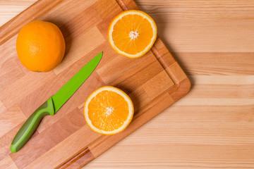 Orange cut into pieces on a wooden board with a green knife