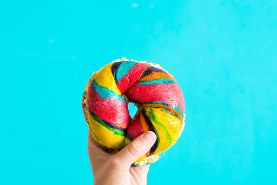 Colorful bagel with cheese and sprinkles in hand on blue background

