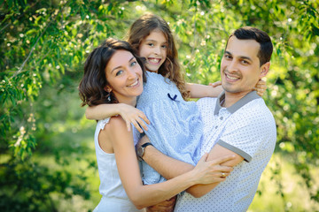 Naklejka premium Young happy family three daughter mother and father hug each other in the park