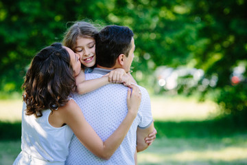 Young happy family three daughter mother and father hug each other in the park