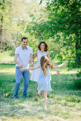 Fototapeta premium Young happy family three daughter run to her parents mother and father in the park