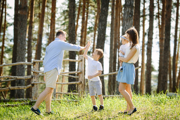 Family portrait of four people mother with daughter and father doing a high-five with son walking in the park near forest