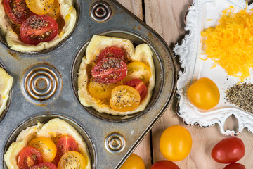 Muffin pan tomato cheese tarts and bowl of shredded cheese.