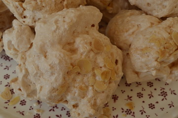 Homemade meringues on brown sugar sprinkled with almond flakes on plate with tiny red flowers
