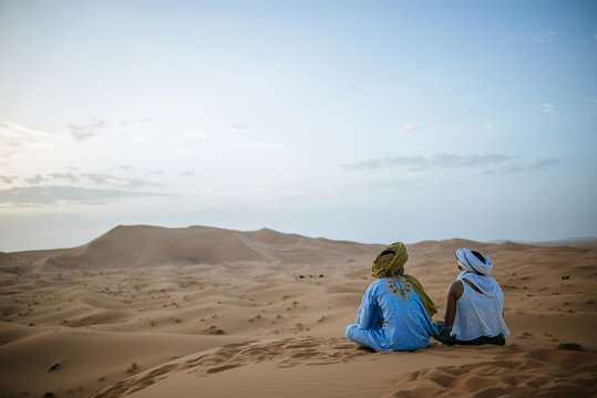 Woman sitting in the desert with Berber guide, watching sunset
