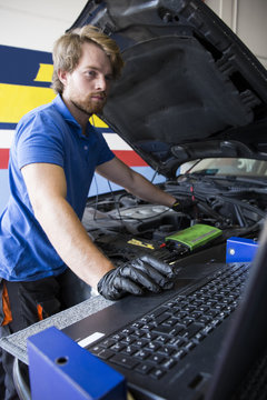 Mechanic fixing a car engine while using a computer in his workshop
