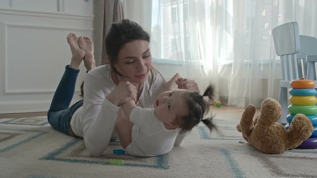 Lovely Young Mom Lying On The Carpet In Kids Room And Playing With Her Little Baby Girl