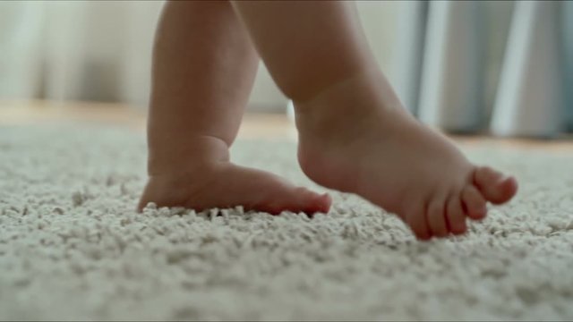 Closeup of little barefoot legs of baby making first steps on comfy rug by herself