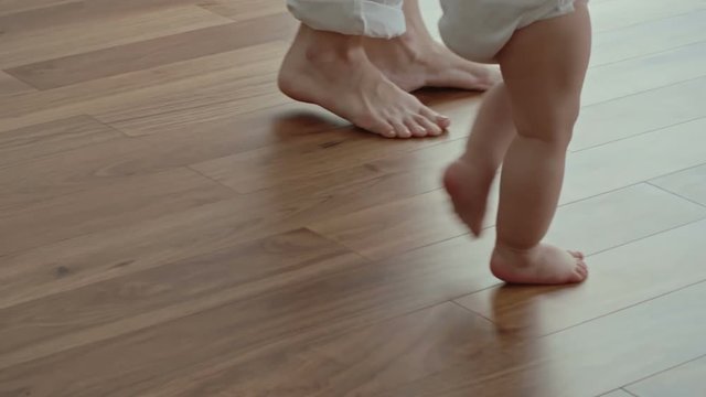 Closeup of legs little baby wearing diaper and walking barefoot together with mom on the floor at home